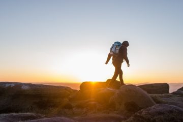 silhouette of man carrying backpack walking on stones